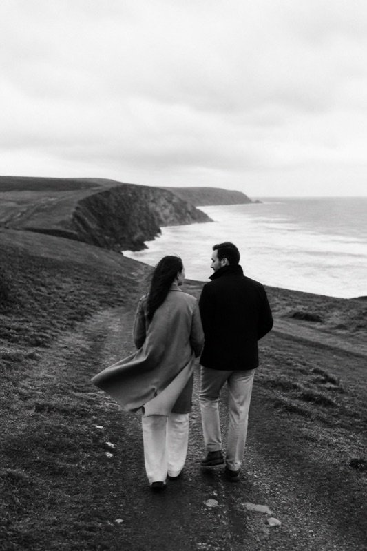A couple walking together along a windswept coastal path.