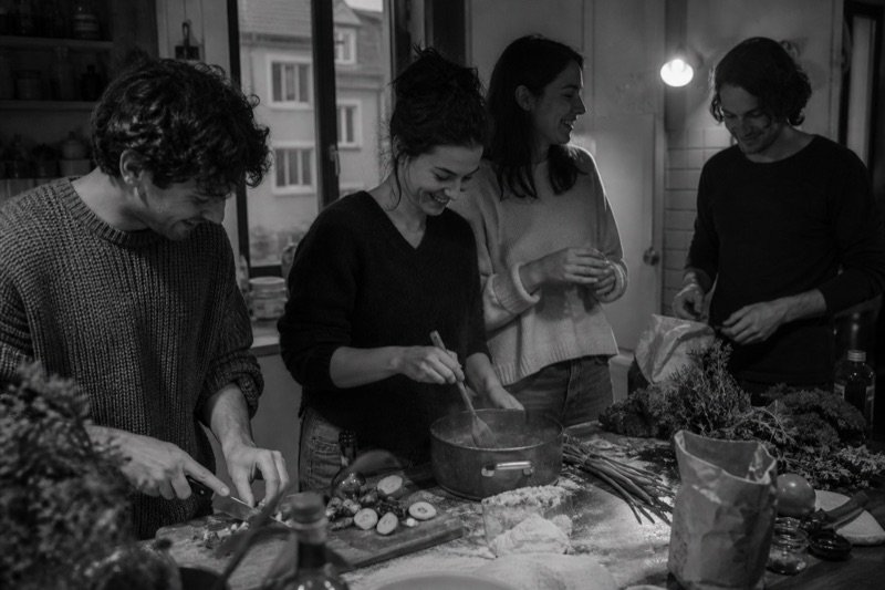 Four friends talking and laughing while cooking together.